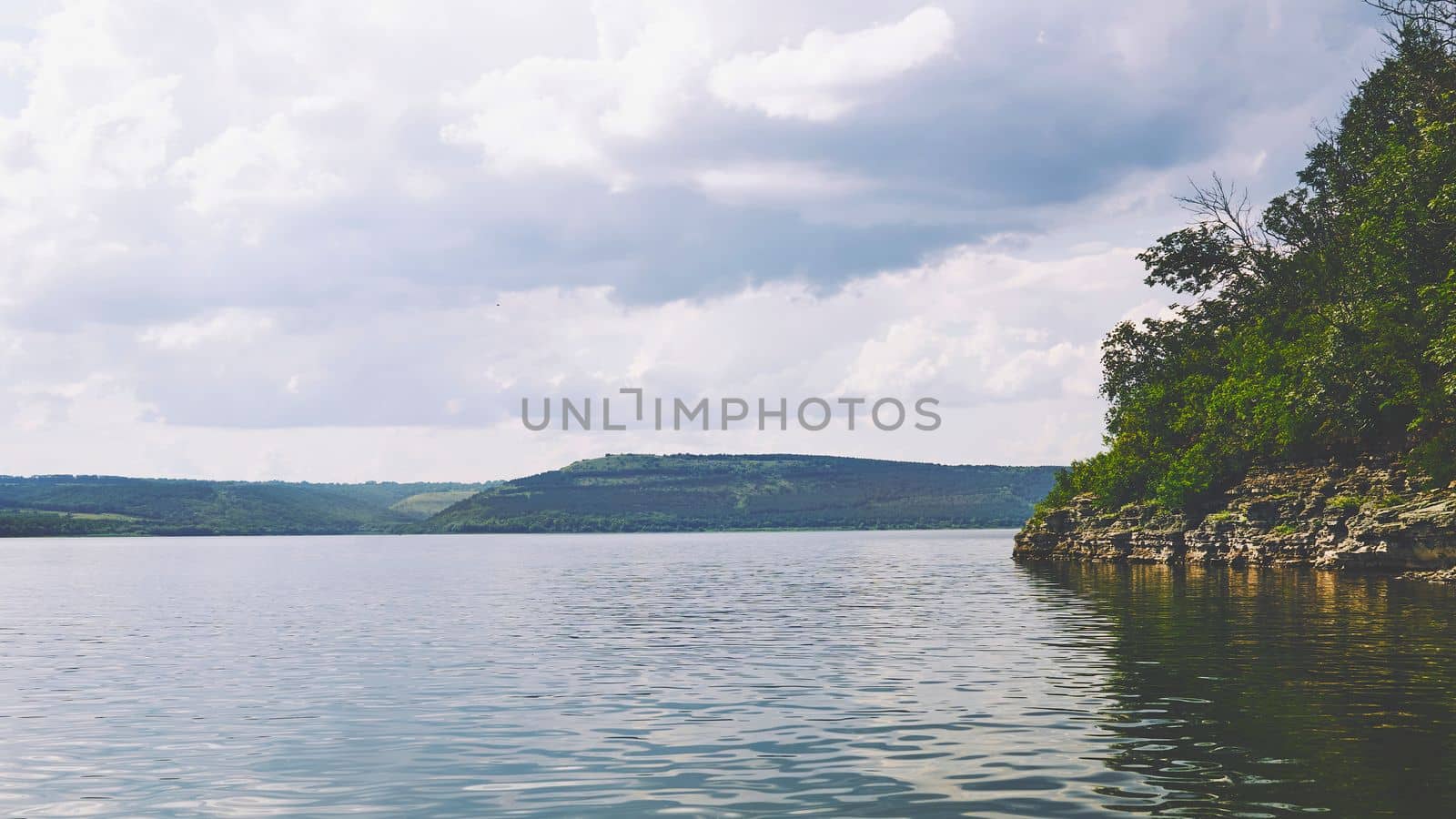 a large natural stream of water flowing in a channel to the sea, a lake, or another such stream. Summer river flowing among lush green rocky hills. Tovtry National Park Ukraine