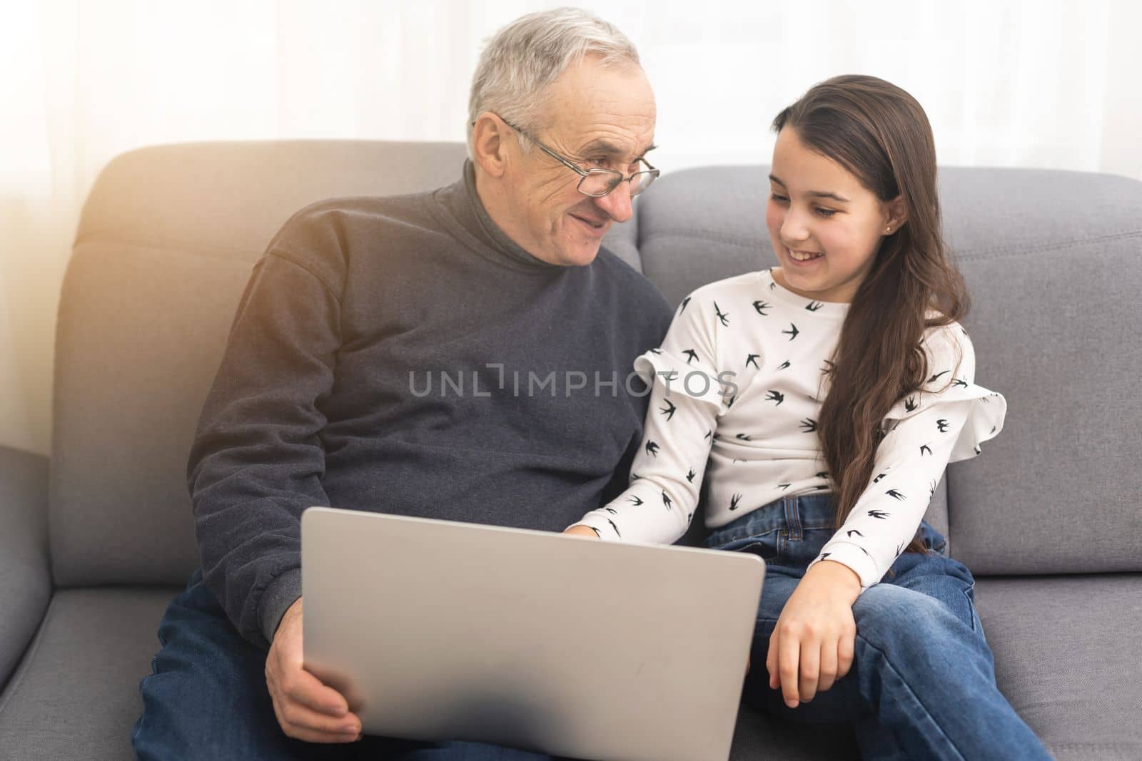 Adorable little girl and happy grandfather using laptop at home by Andelov13