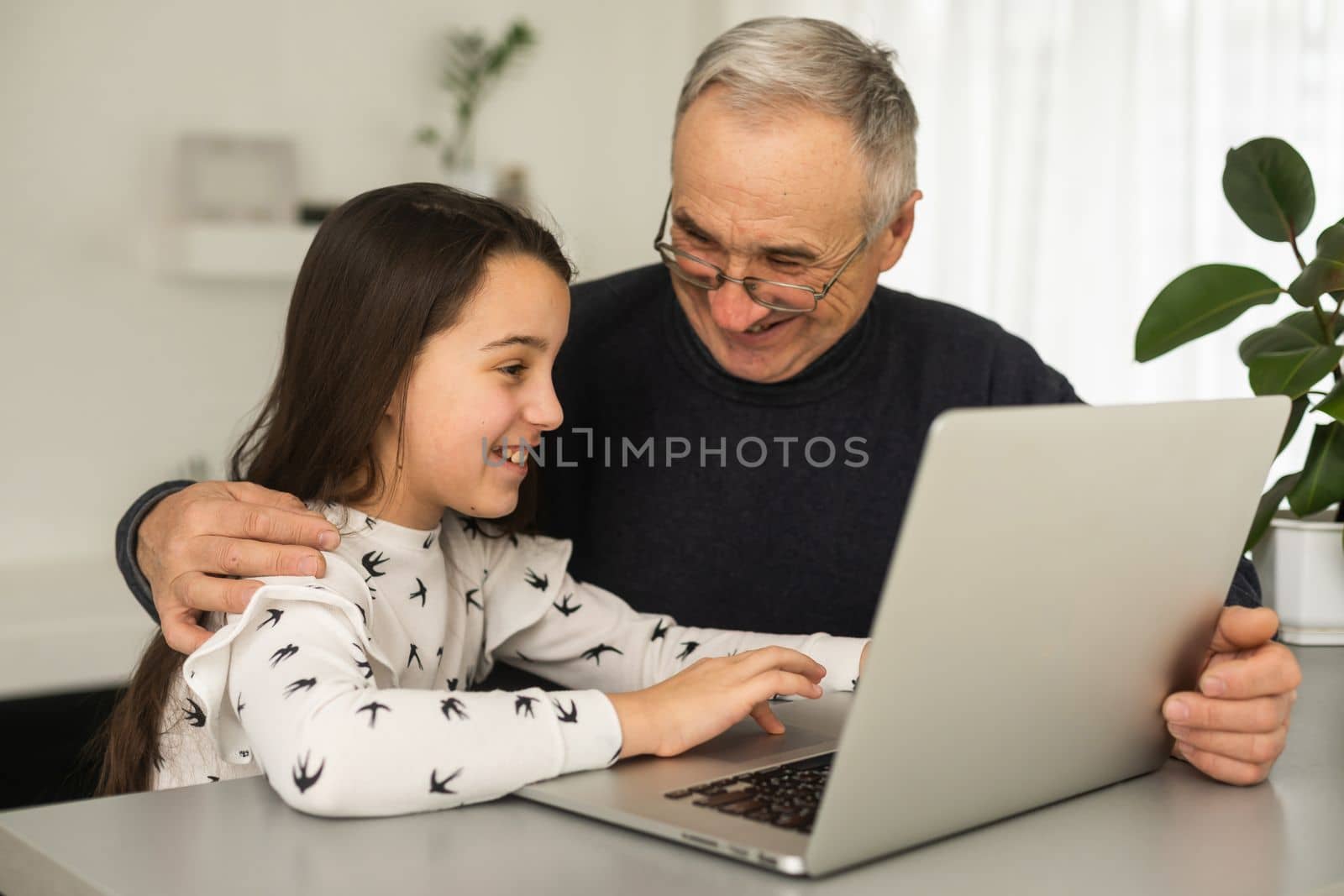 Happy retirement grandfather and pretty granddaughter laughing while watching e-book for learning to education together by laptop. Family educational at home concept. Technology and education