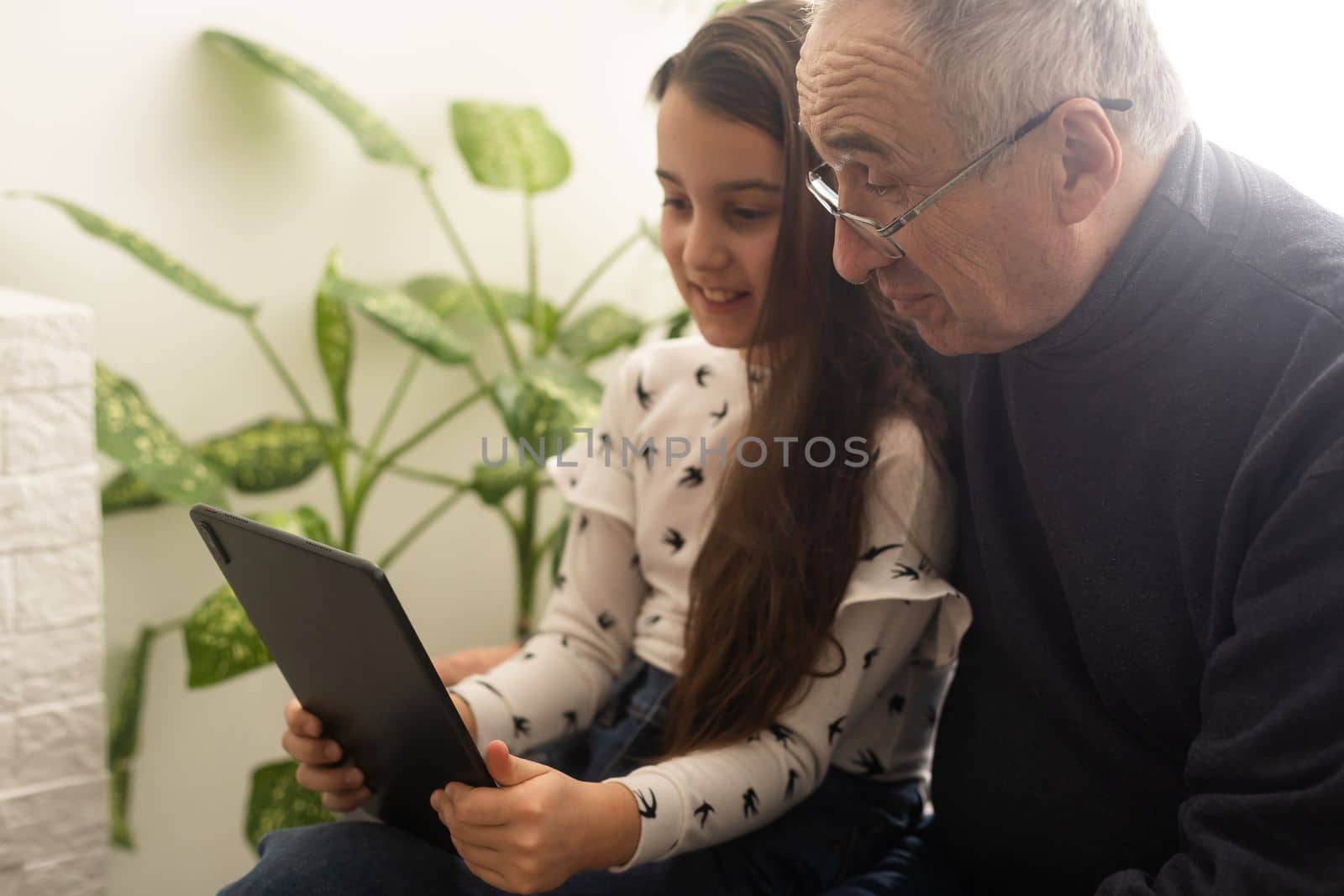 Senior man with his grandchild looking together on photos in tablet by Andelov13