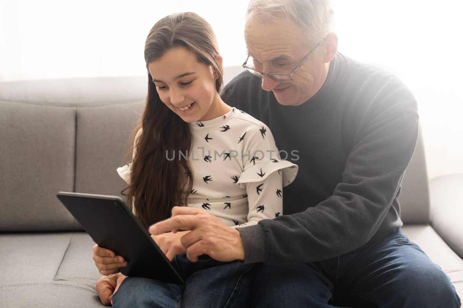 Happy family senior grandfather and girl watching cartoon on tablet on weekend day at home together by Andelov13