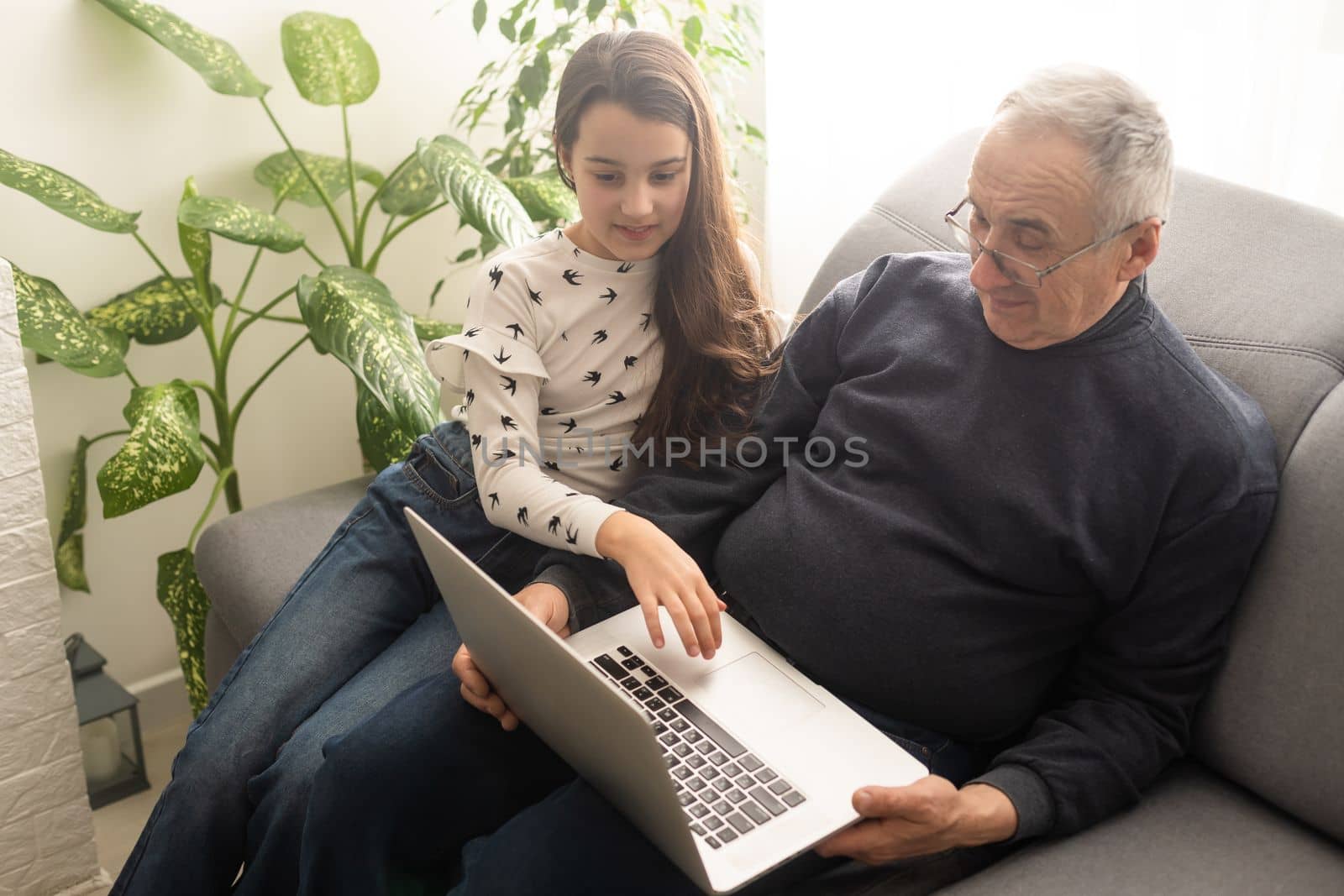 Happy retirement grandfather and pretty granddaughter laughing while watching e-book for learning to education together by laptop. Family educational at home concept. Technology and education. by Andelov13