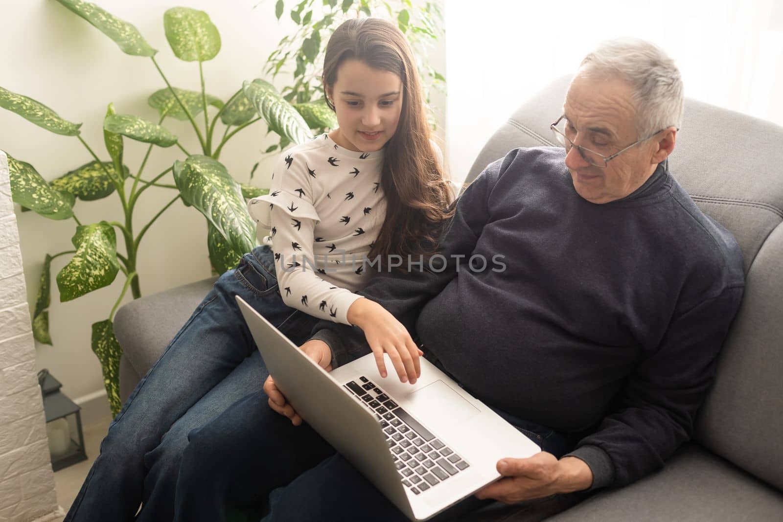 Happy retirement grandfather and pretty granddaughter laughing while watching e-book for learning to education together by laptop. Family educational at home concept. Technology and education