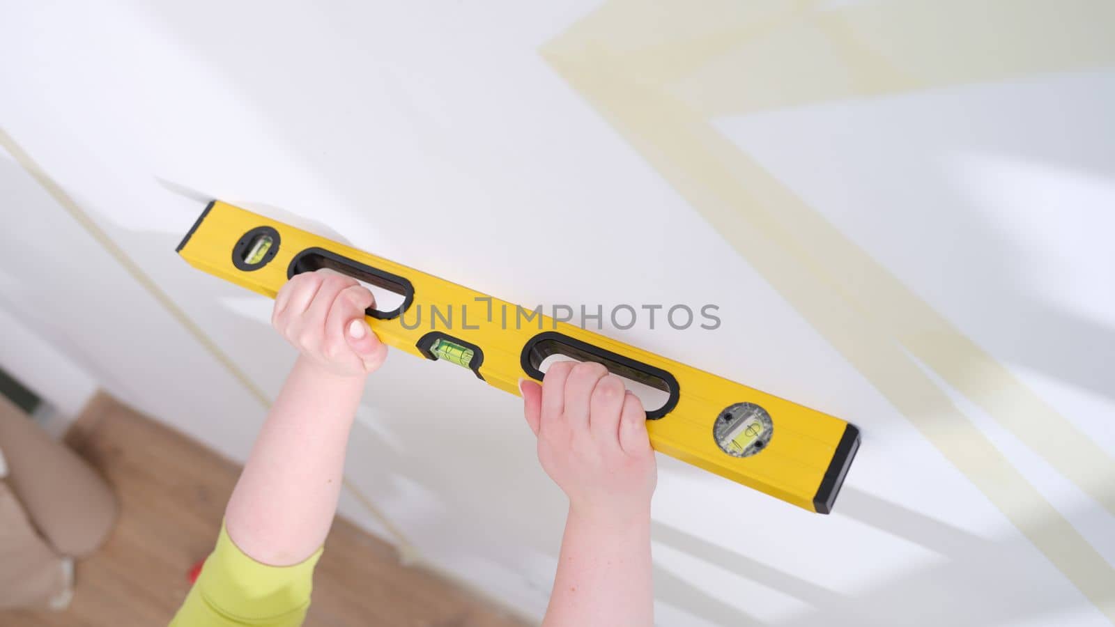 Hands of worker hold yellow level against white wall. Home craftsman and the evenness of walls concept