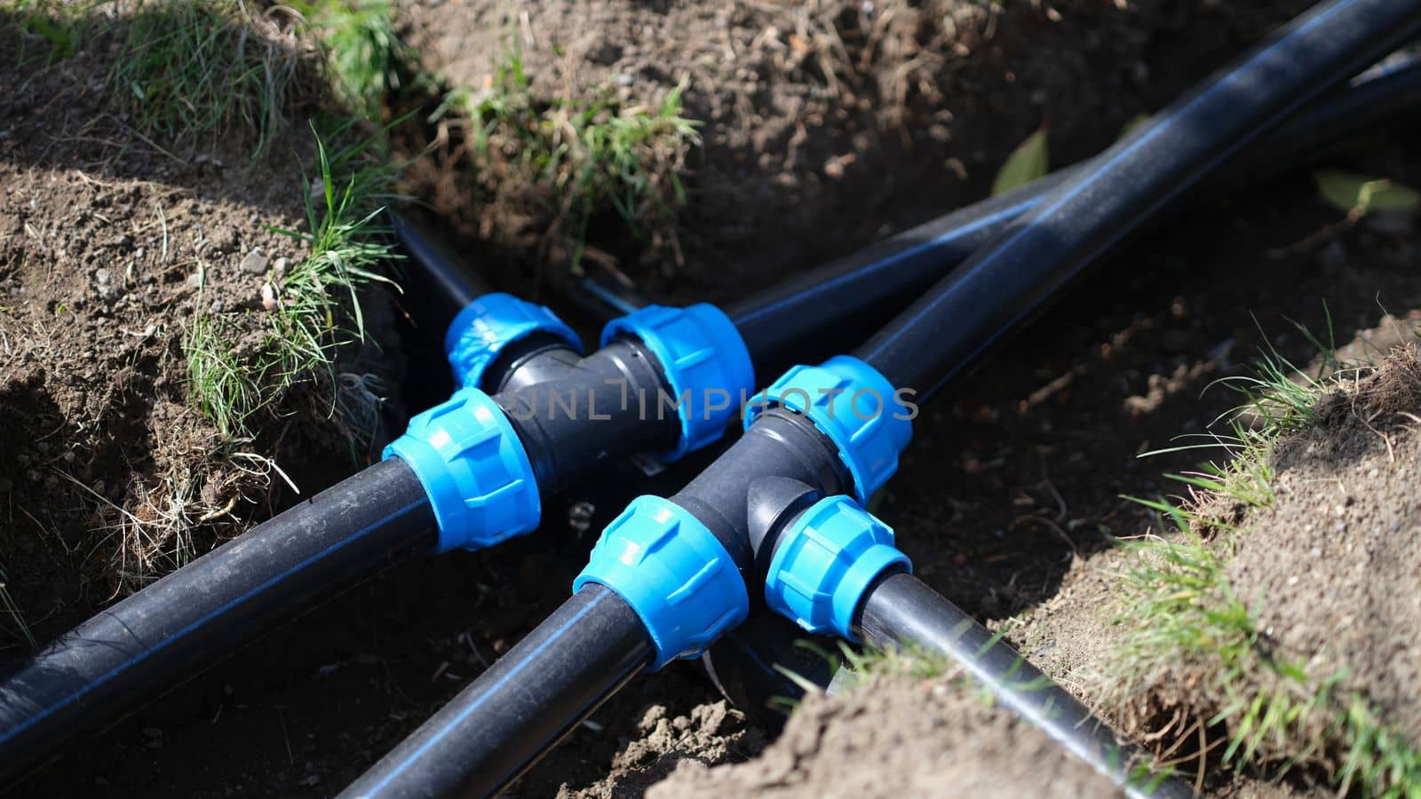 Black long pipe lies and tee adapter in dug-out earth closeup by kuprevich