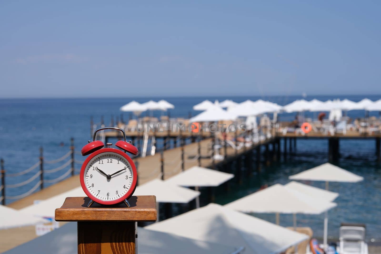 Alarm clock for ten o'clock on beach with jetty and umbrellas by kuprevich