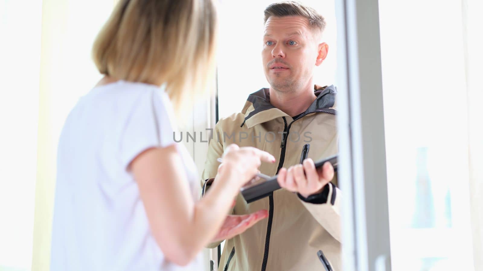 Male courier holds tablet and writes down data of female client at door of house by kuprevich