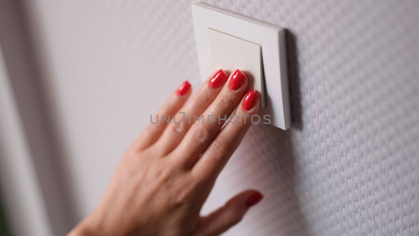 Female hand presses white switch on gray wall closeup. Saving electricity at home concept