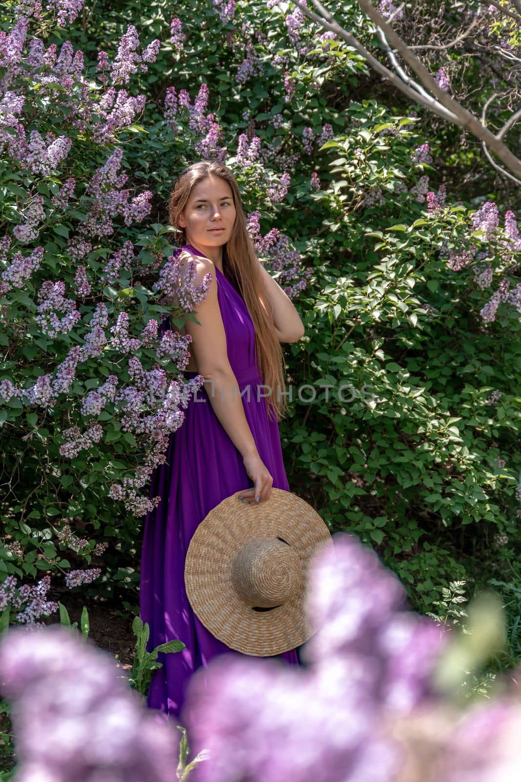 portrait of young woman with long hair outdoors in blooming lilac garden.