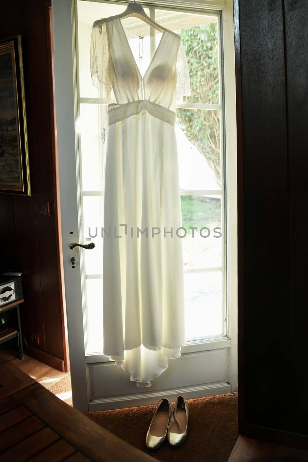 The Wedding dress hanging on the door and golden shoes