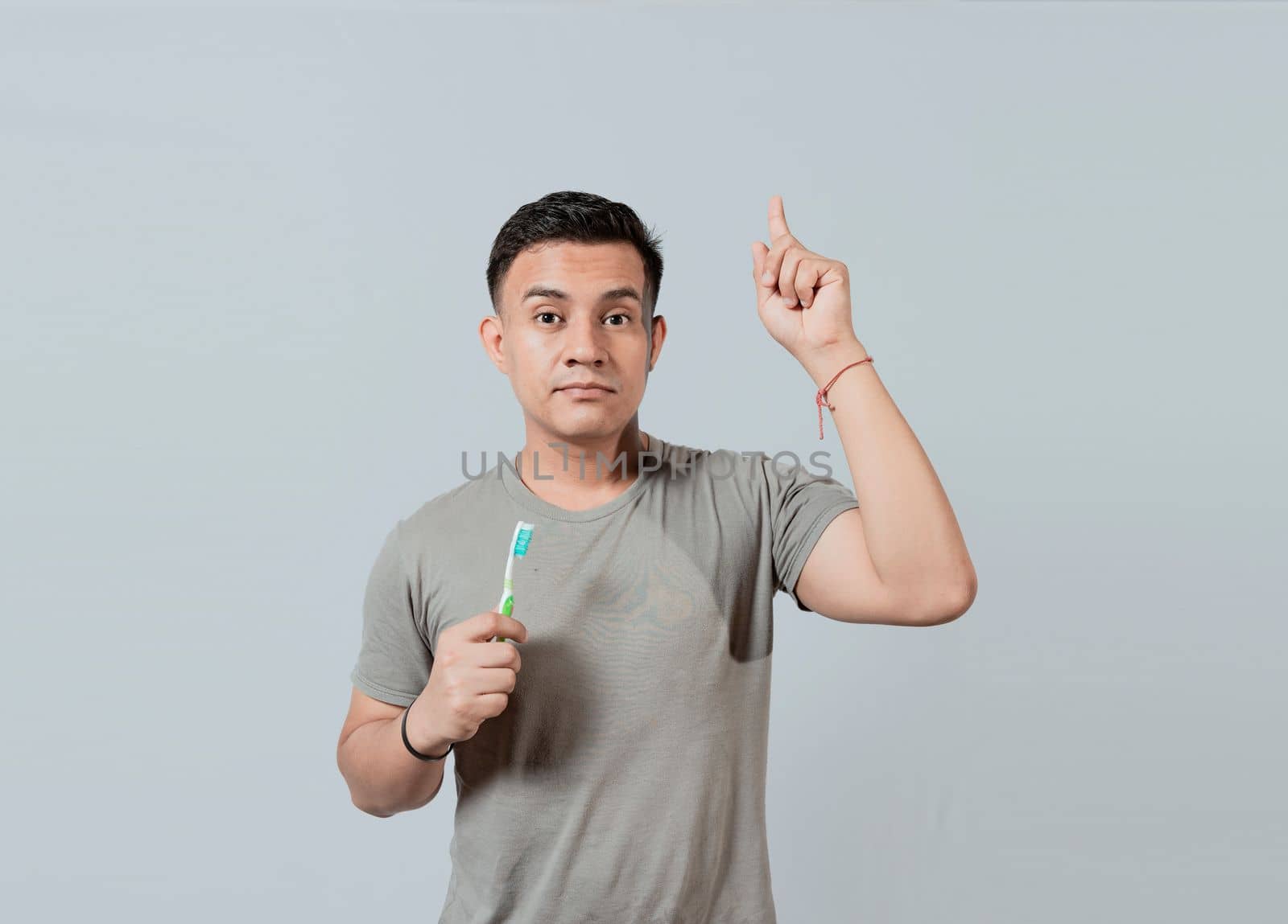 Handsome guy holding toothbrush pointing an advertisement up. Caucasian handsome man holding toothbrush pointing up. People holding toothbrush pointing a promo up by isaiphoto