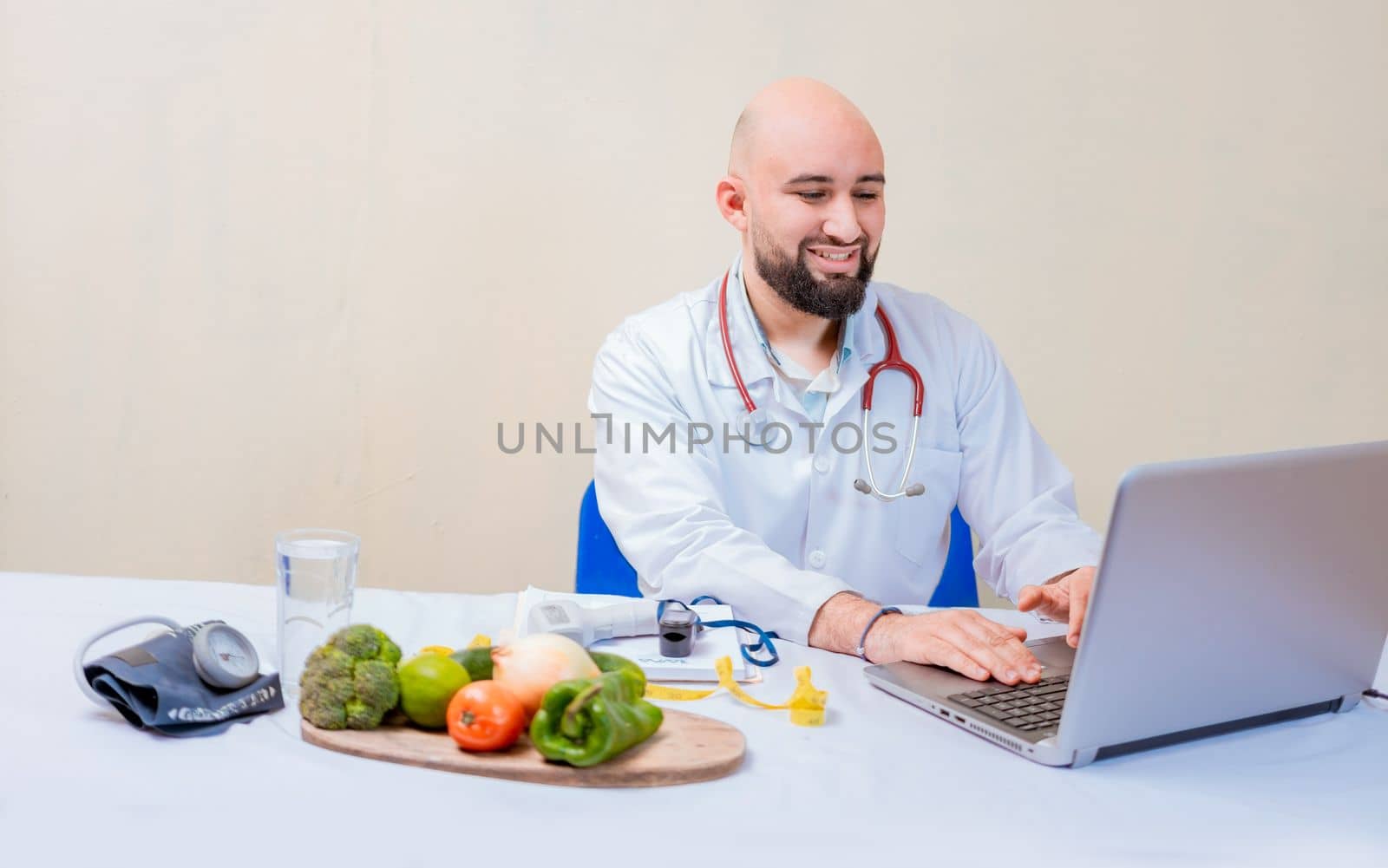 Nutritionist doctor using laptop at workplace. Bearded nutritionist doctor working on laptop at desk, Smiling nutritionist with laptop at desk by isaiphoto