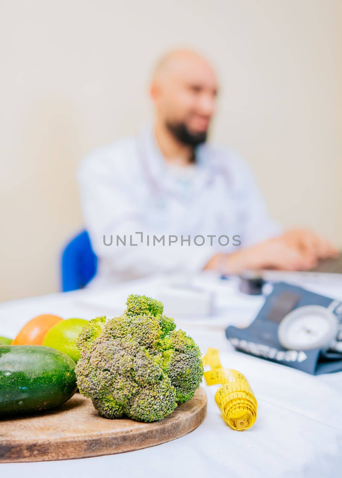 Focus on vegetables of nutritionist with laptop at the desk. Nutritionist working on laptop, giving online consultation to client at clinic, focus on vegetables by isaiphoto