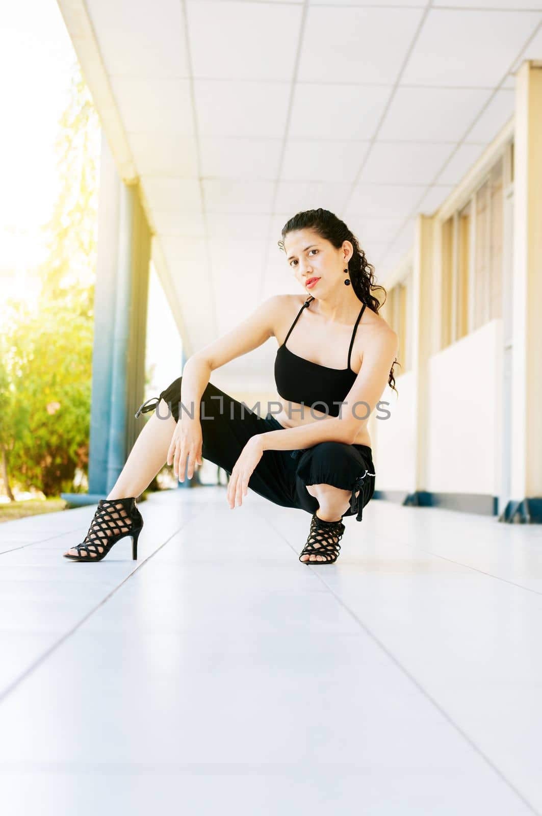 Dance artist woman in high heels outdoors. Portrait of dance girl in high heels crouching on the floor. Portrait of dancer Woman in heels on the floor looking at the camera.
