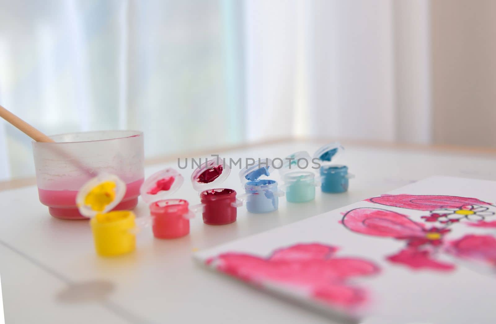 Palette with multicolor paints and water with a brush for children