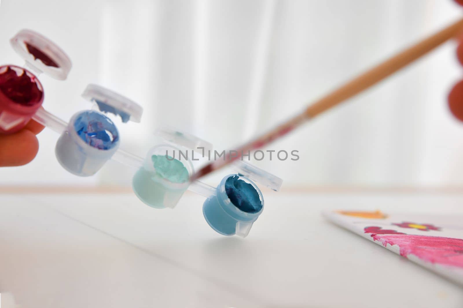 Palette with multicolor paints and water with a brush for children