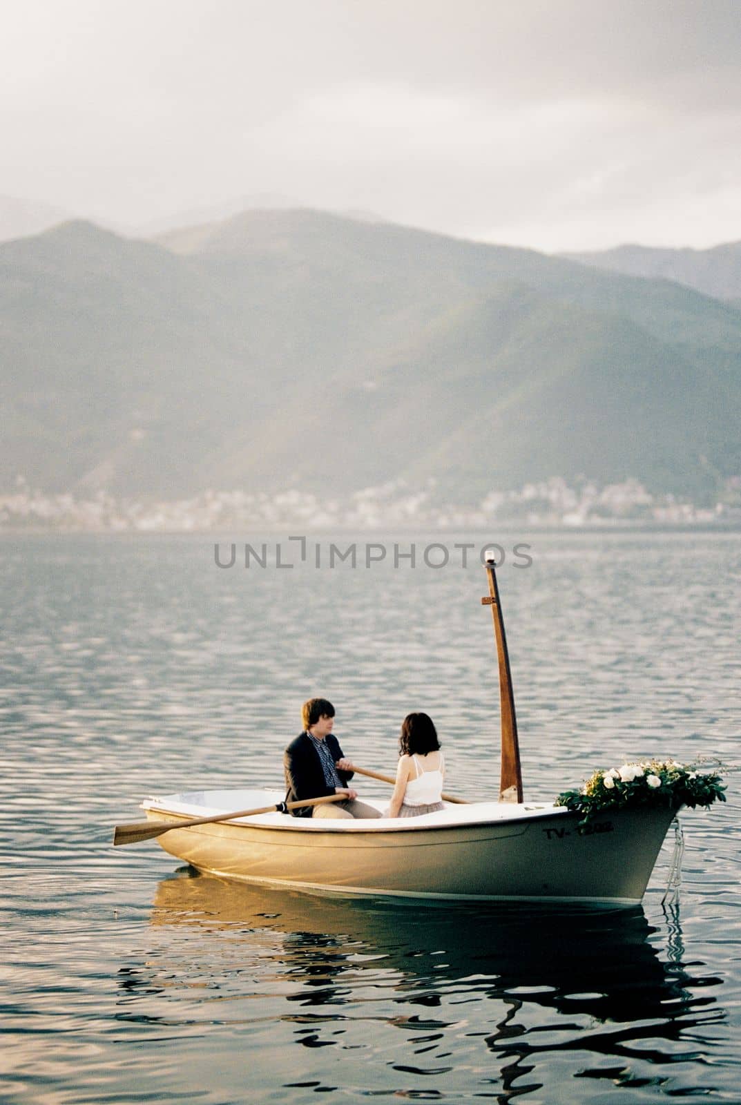 Man and woman are sailing in a boat with oars on the sea against the backdrop of mountains. High quality photo