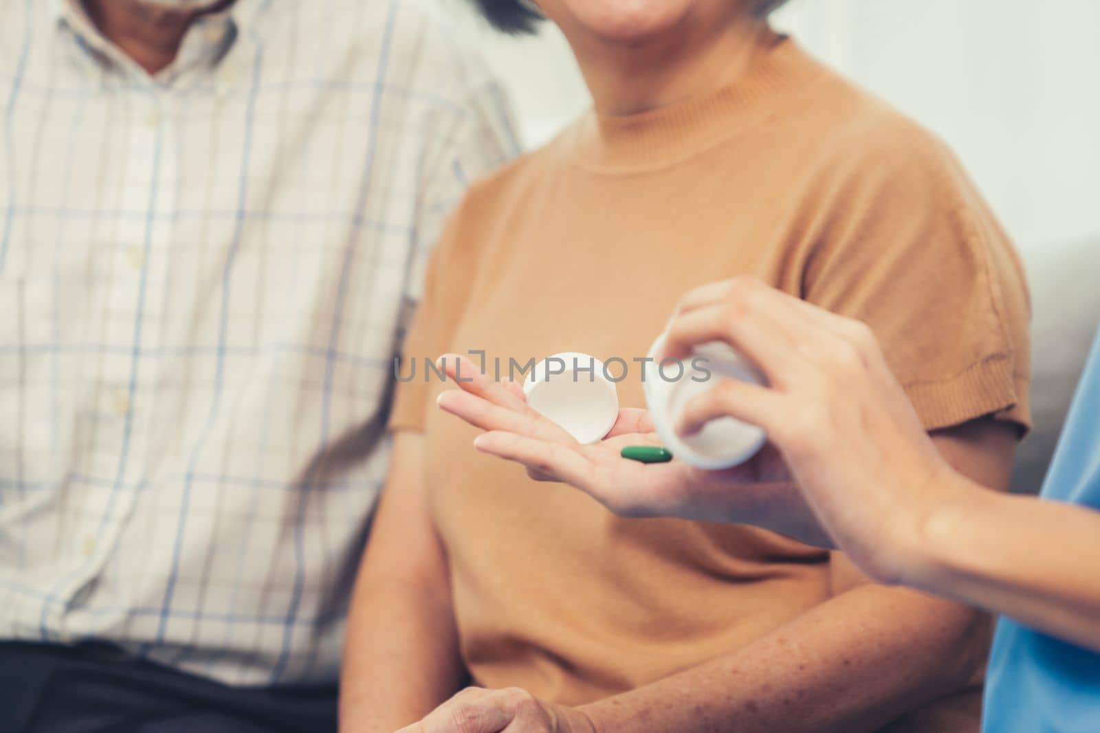 Contented senior woman sit along side with her husband, taking medicines while her caregiver advising her medication. Medication for seniors, nursing house, healthcare at home.