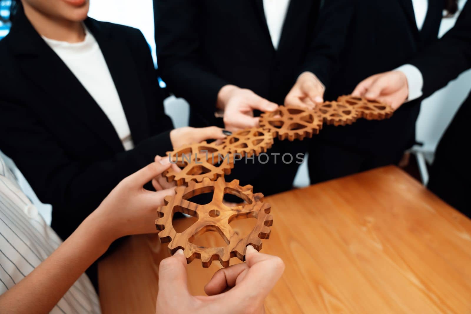 Closeup hand holding wooden gear by businesspeople wearing suit for harmony synergy in office workplace concept. Group of people hand making chain of gears into collective form for unity symbol.