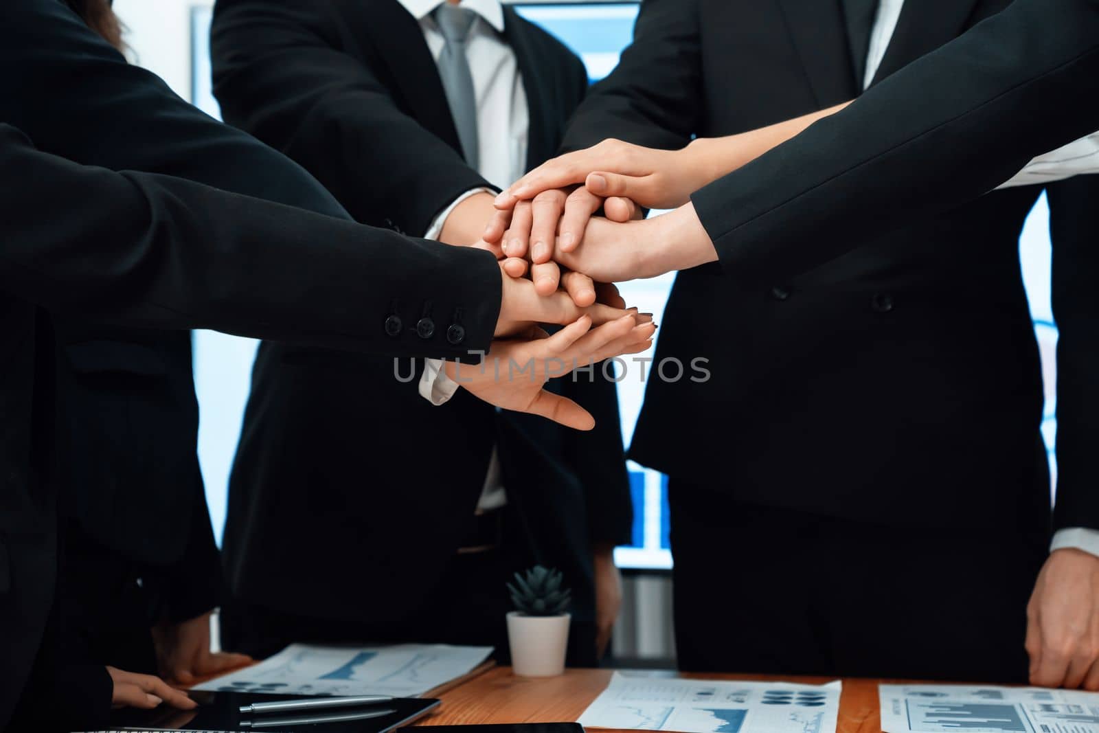 Closeup business team of suit-clad businessmen and women join hand stack together and form circle. Colleague collaborate and work together to promote harmony and teamwork concept in office workplace.