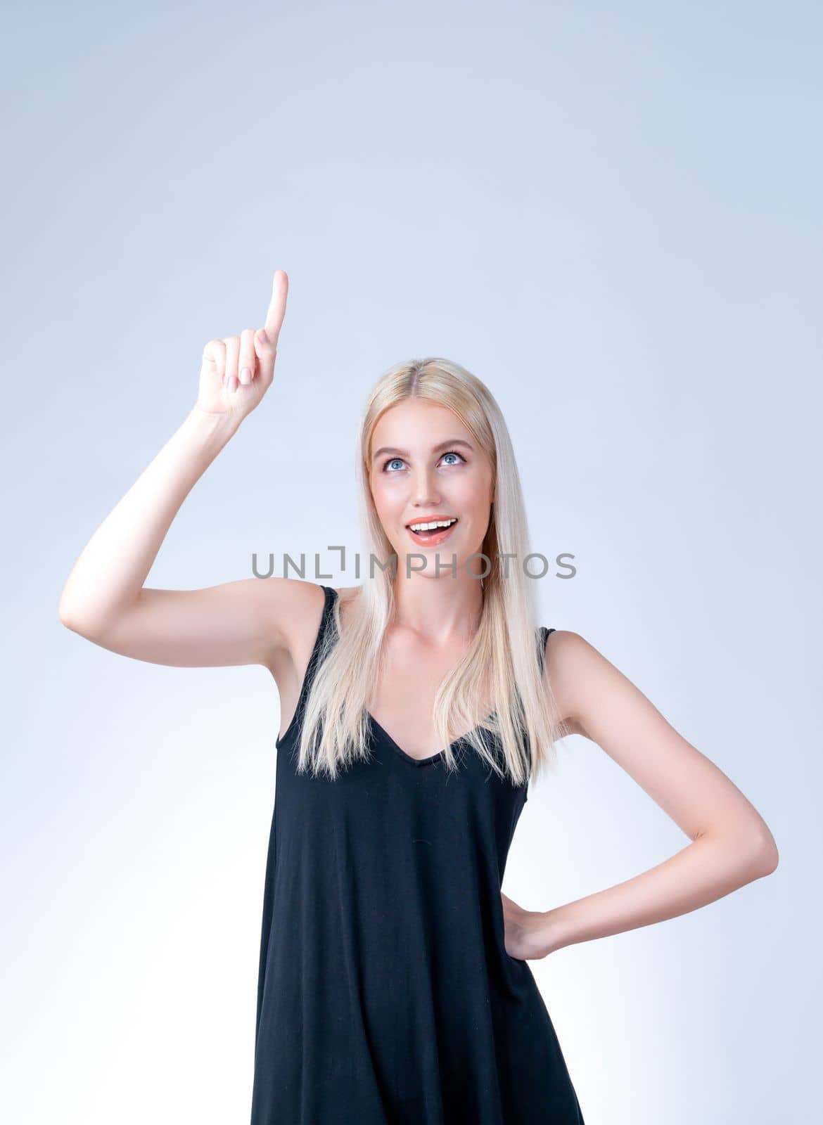 Personable beautiful woman with perfect makeup clean skin pointing finger up in copyspace isolated background. Promotion indicated by hand gesture to show skincare product advertising.