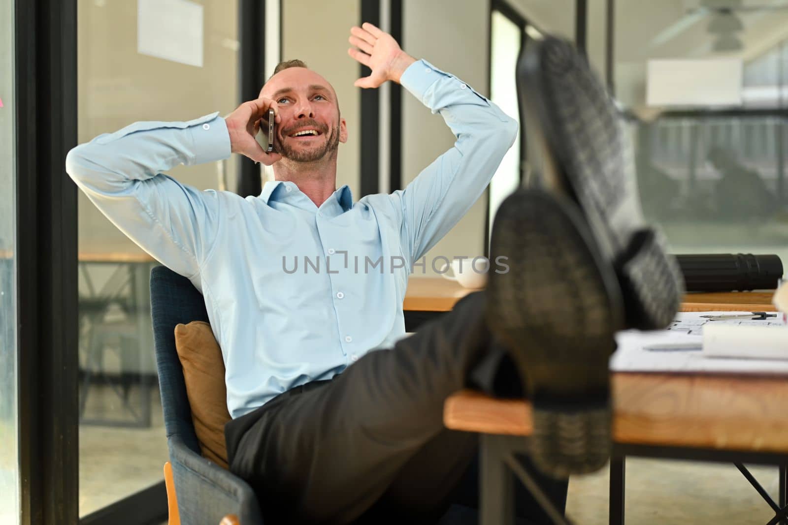 Happy caucasian millennial man chatting with friends distracted from work while relaxing at workplace by prathanchorruangsak