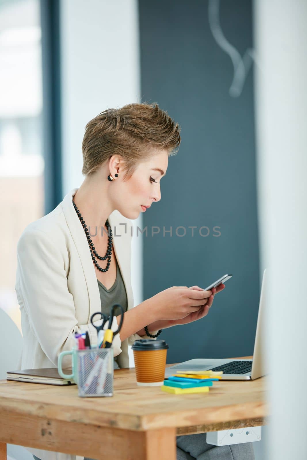 Technology has always been her best business tool. a young businesswoman texting on a cellphone in an office. by YuriArcurs
