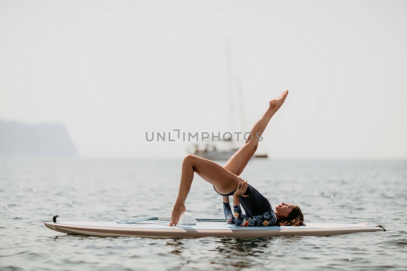 Woman sup yoga. Middle age sporty woman practising yoga pilates on paddle sup surfboard. Female stretching doing workout on sea water. Modern individual hipster outdoor summer sport activity