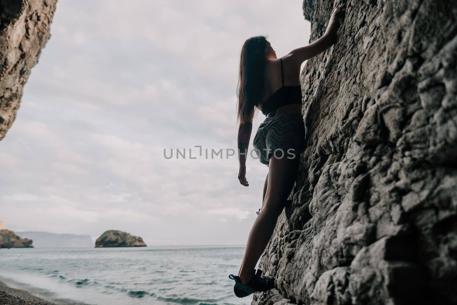 A girl climbs a rock. The athlete trains in nature. Woman overcomes difficult climbing route. Extreme hobby. Tourist woman rock climber hiking on mountains rocks over beautiful sea coast