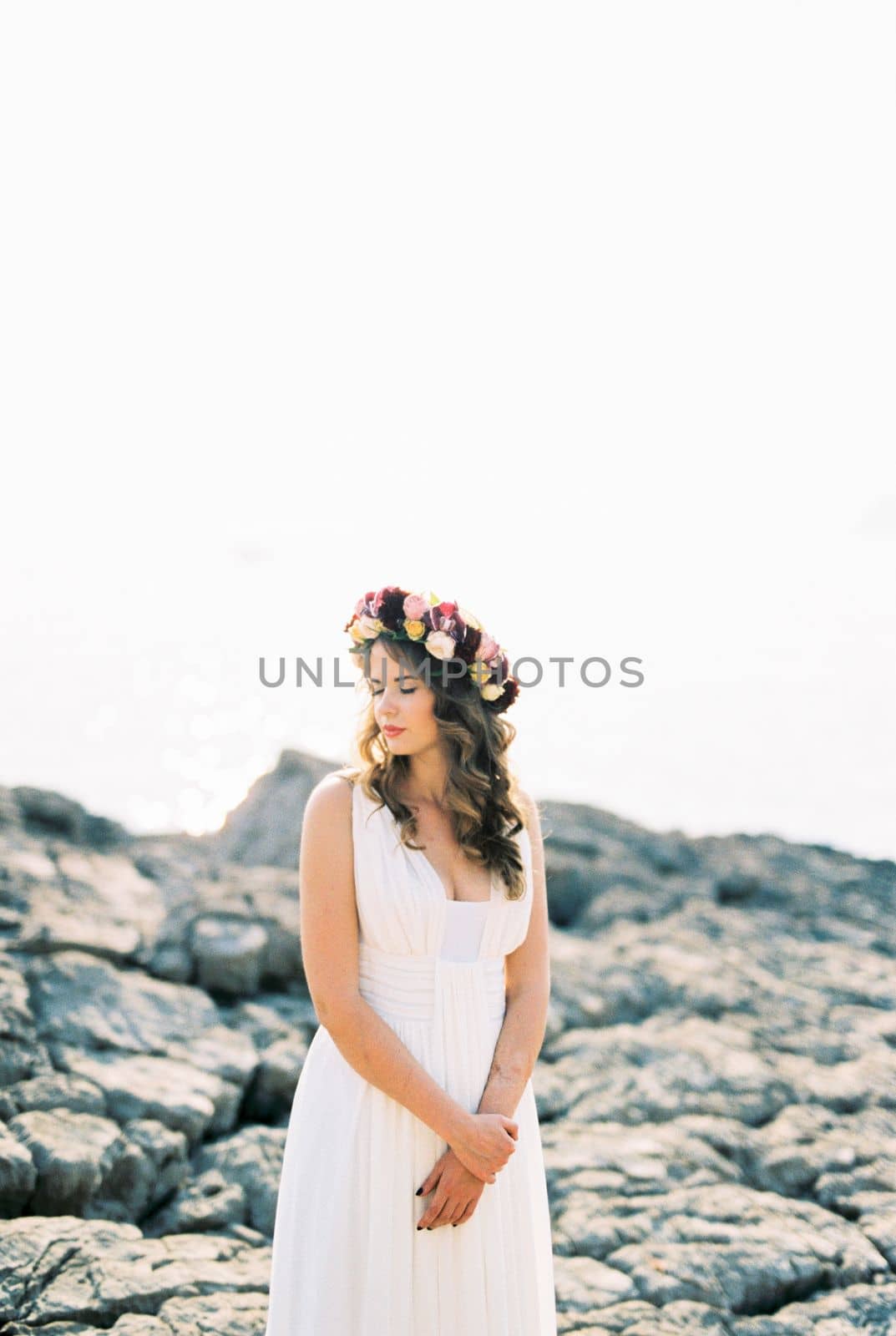 Bride in a colorful wreath stands on a rocky shore. High quality photo