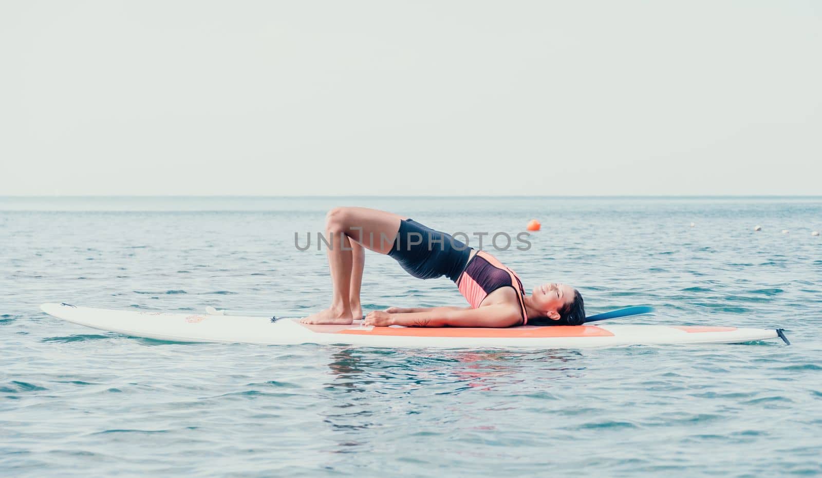 Woman sup yoga. Happy young sporty woman practising yoga pilates on paddle sup surfboard. Female stretching doing workout on sea water. Modern individual female outdoor summer sport activity