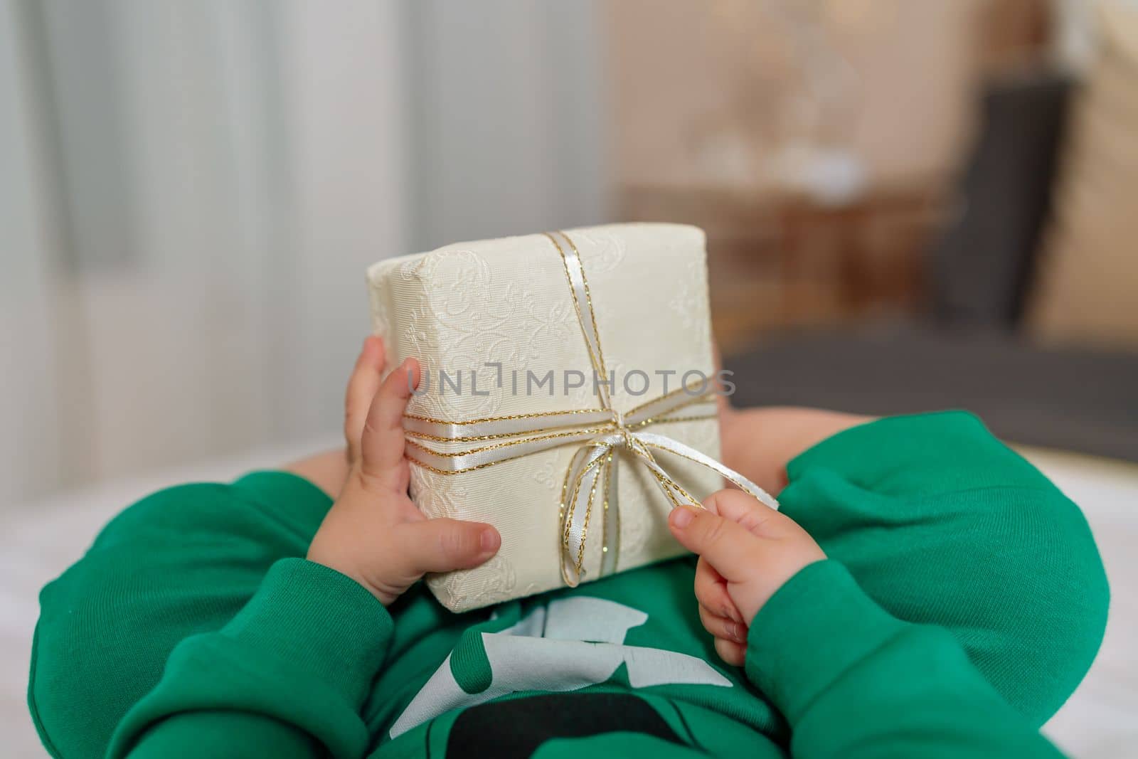 Kid gift. A little boy in a green suit holds a gift box with his feet and hands in bed