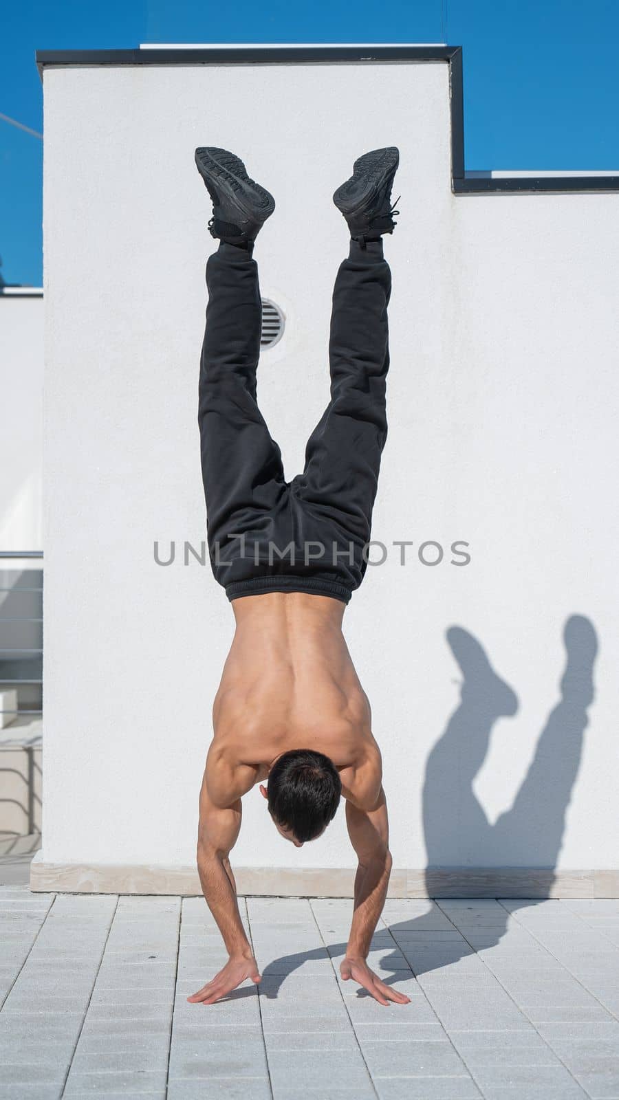 Man doing a handstand outdoors against a white wall