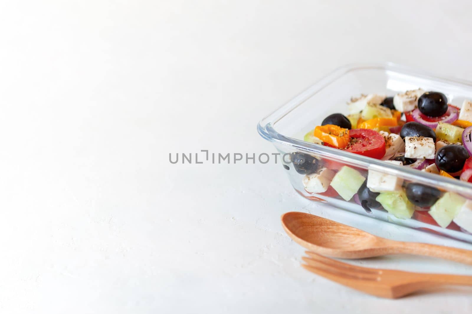 lunch box with greek salad, reusable glass container, wooden cutlery, on white background, side view, copy space