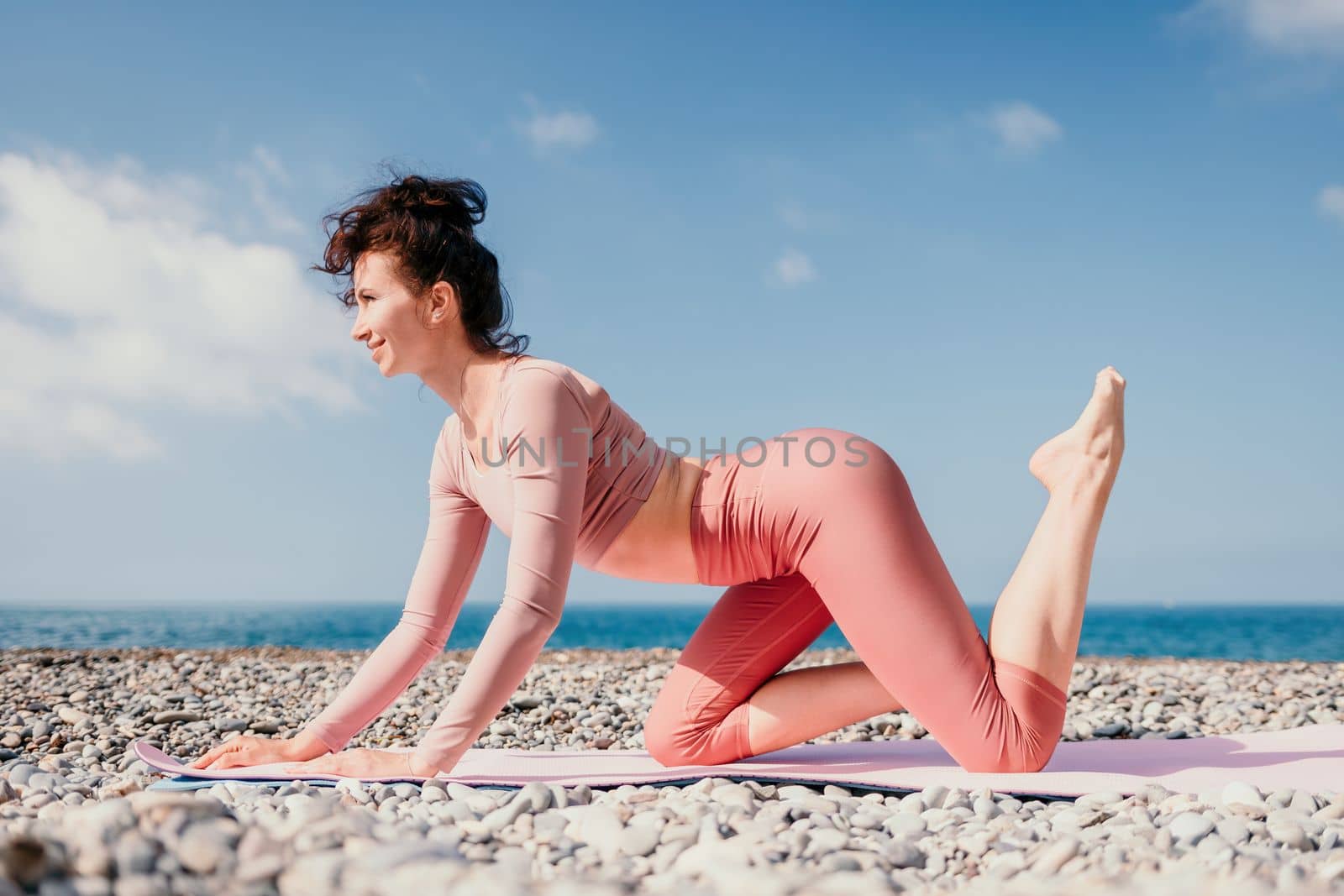 Middle aged well looking woman with black hair doing Pilates with the ring on the yoga mat near the sea on the pebble beach. Female fitness yoga concept. Healthy lifestyle, harmony and meditation.