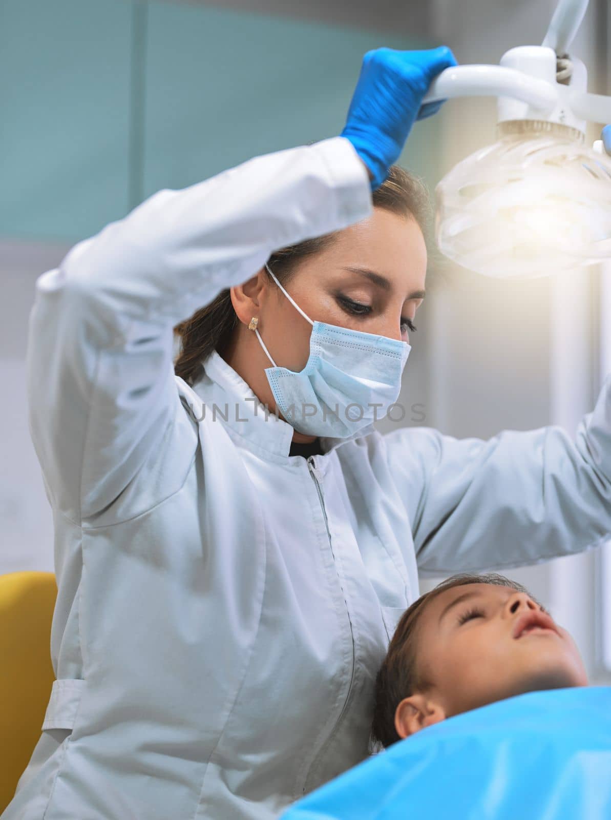 Try not to look at the light. a focused young female dentist wearing a surgical mask whos about to give a checkup on her young little patient