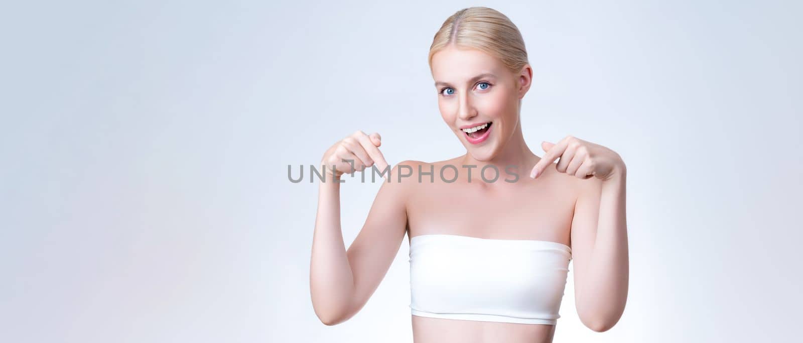 Personable beautiful woman with perfect makeup clean skin pointing finger in copyspace isolated background. Promotion indicated by hand gesture concept for skincare product advertisement.