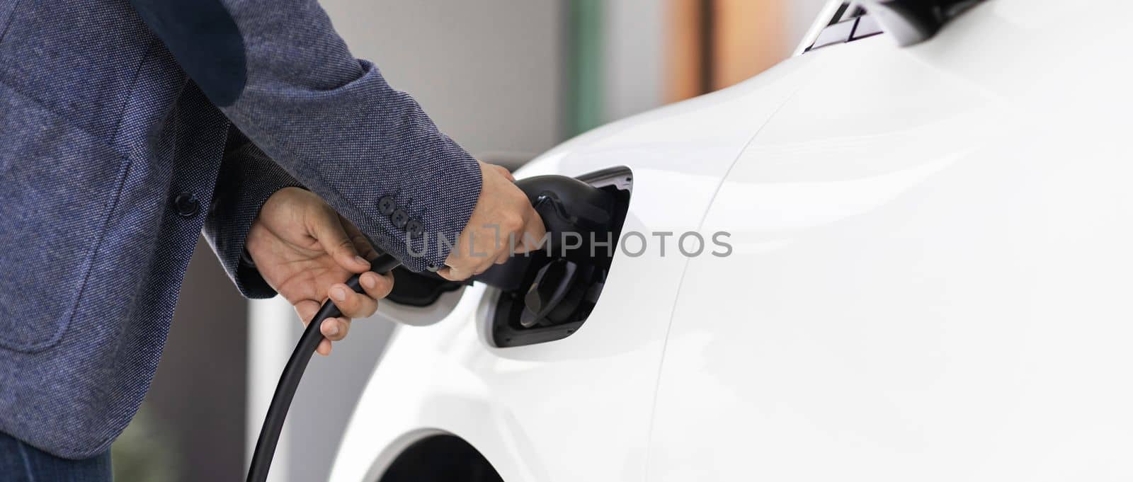 Closeup progressive asian man install cable plug to his electric car with home charging station. Concept of the use of electric vehicles in a progressive lifestyle contributes to clean environment.