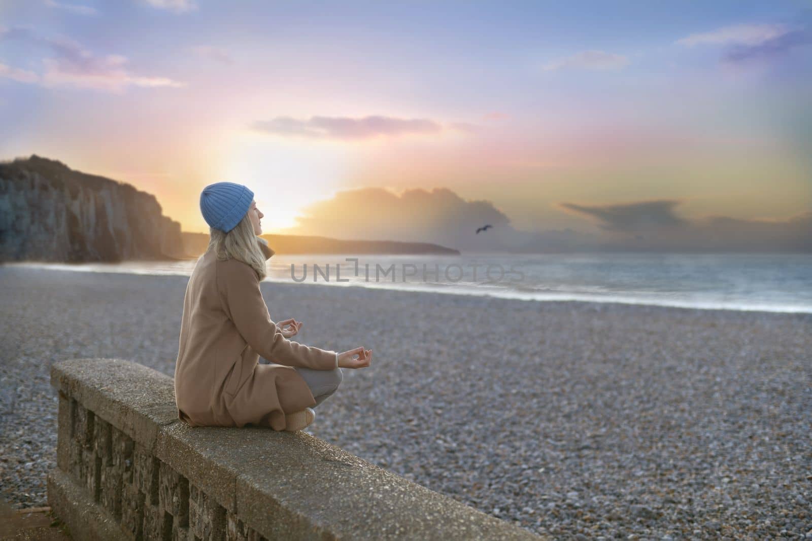 A woman meditates against the backdrop of alabaster rocks and the atlantic ocean by Godi