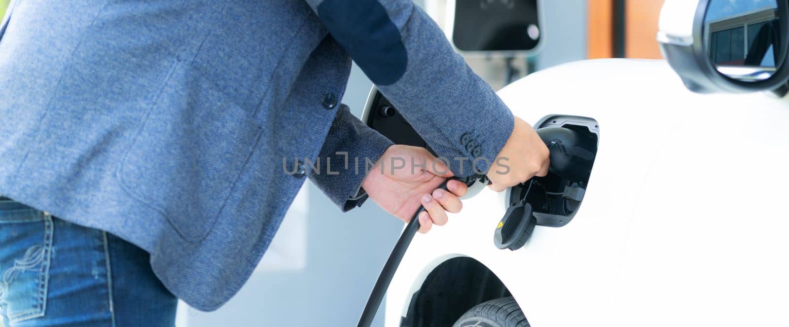 Progressive asian man recharge his EV car at home charging station. by biancoblue