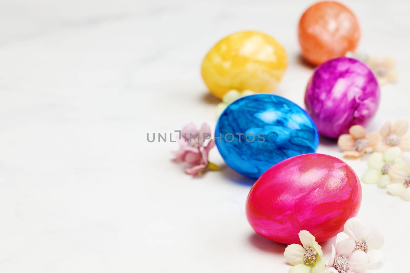 Easter eggs painted in pastel colors on a white background with copy space and cute spring flowers, Happy Easter Holiday concept with space for text. Yellow pink and blue bright colors