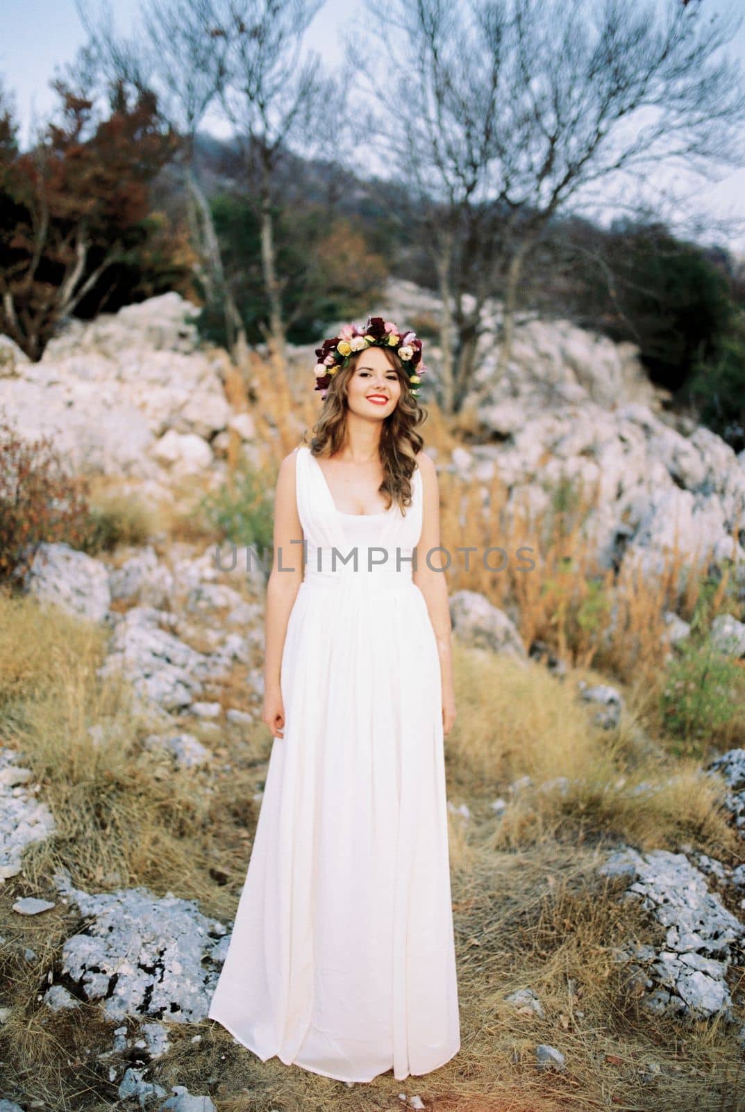 Smiling bride in a multi-colored wreath stands on a mountain among the stones. High quality photo