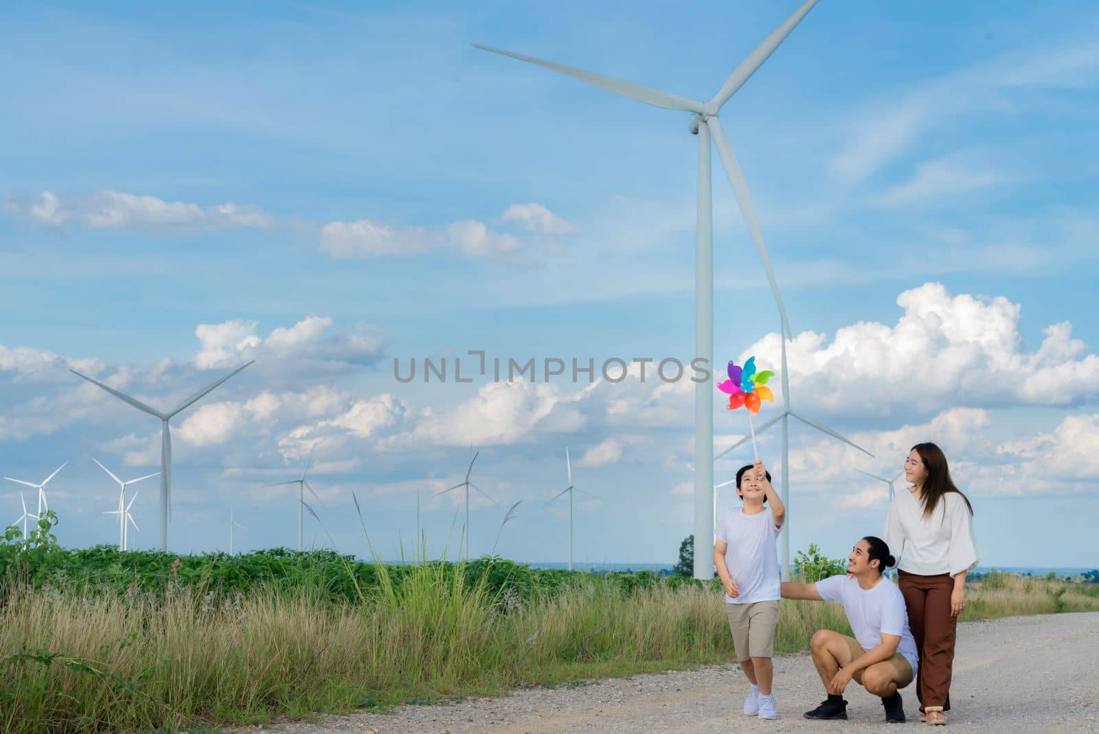 Progressive happy family enjoying their time at wind farm for green energy production concept. Wind turbine generators provide clean renewable energy for eco-friendly purposes.