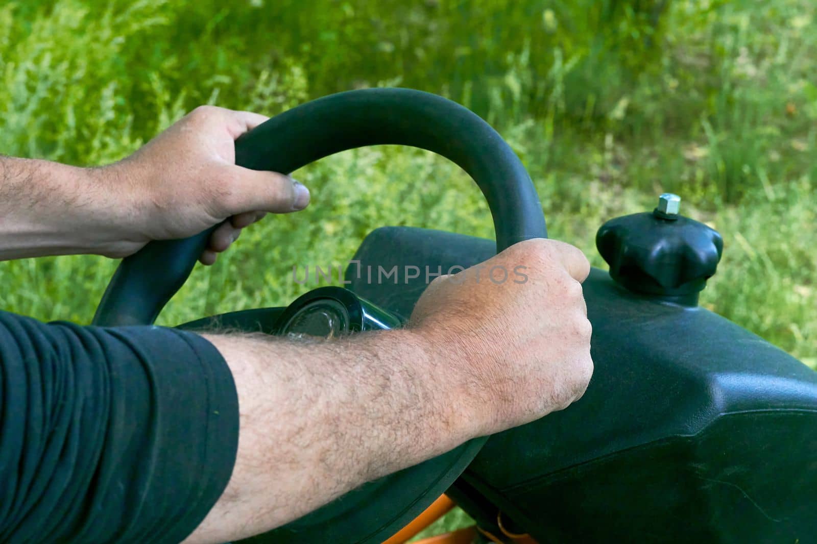 a wheel that a driver rotates in order to steer a vehicle. Male hands of the driver holding the steering wheel of a tractor, lawn mower