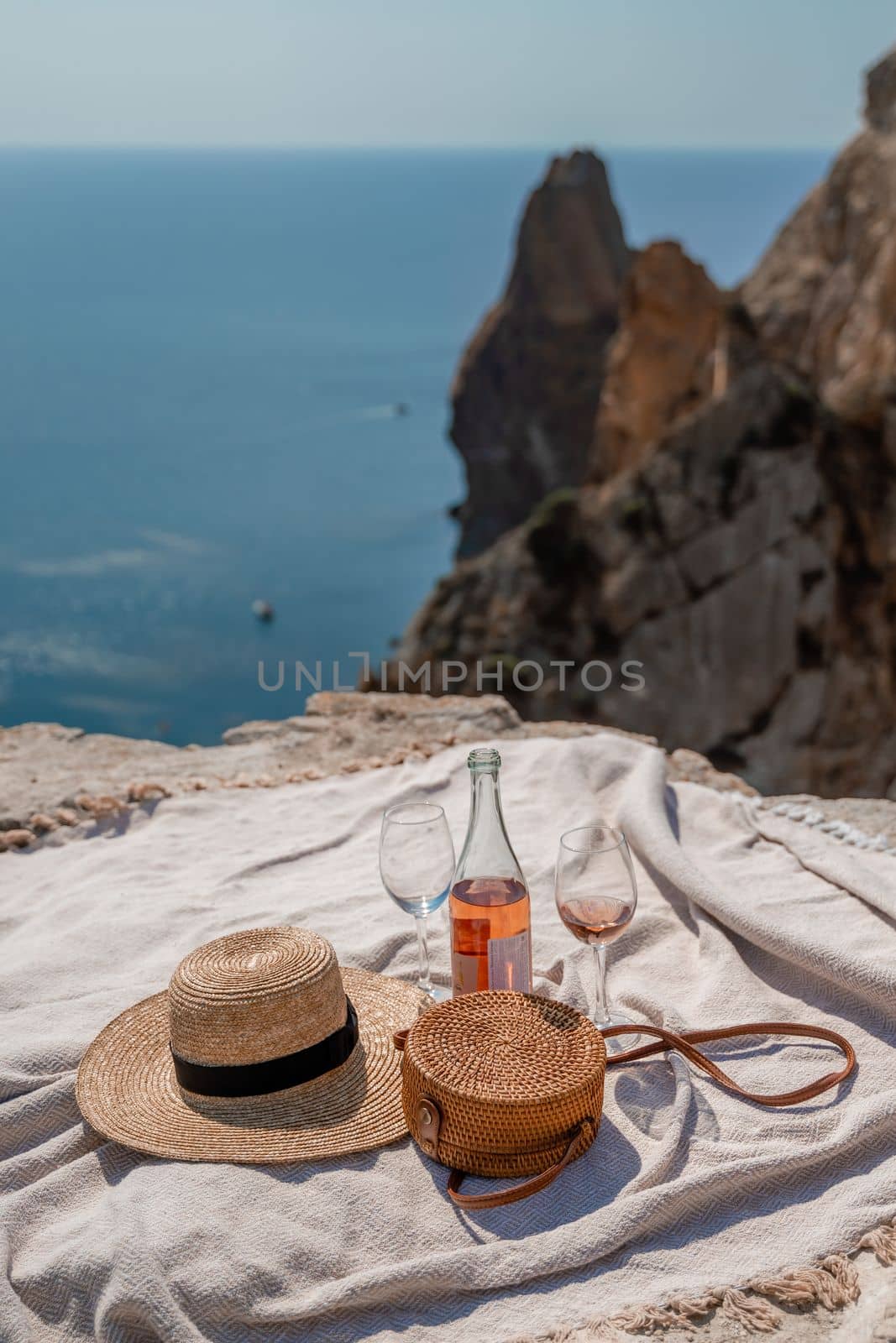 A picnic blanket, champagne, two glasses, a hat and a straw purse. Top on the mountain against the background of the sea and rocks in the sea