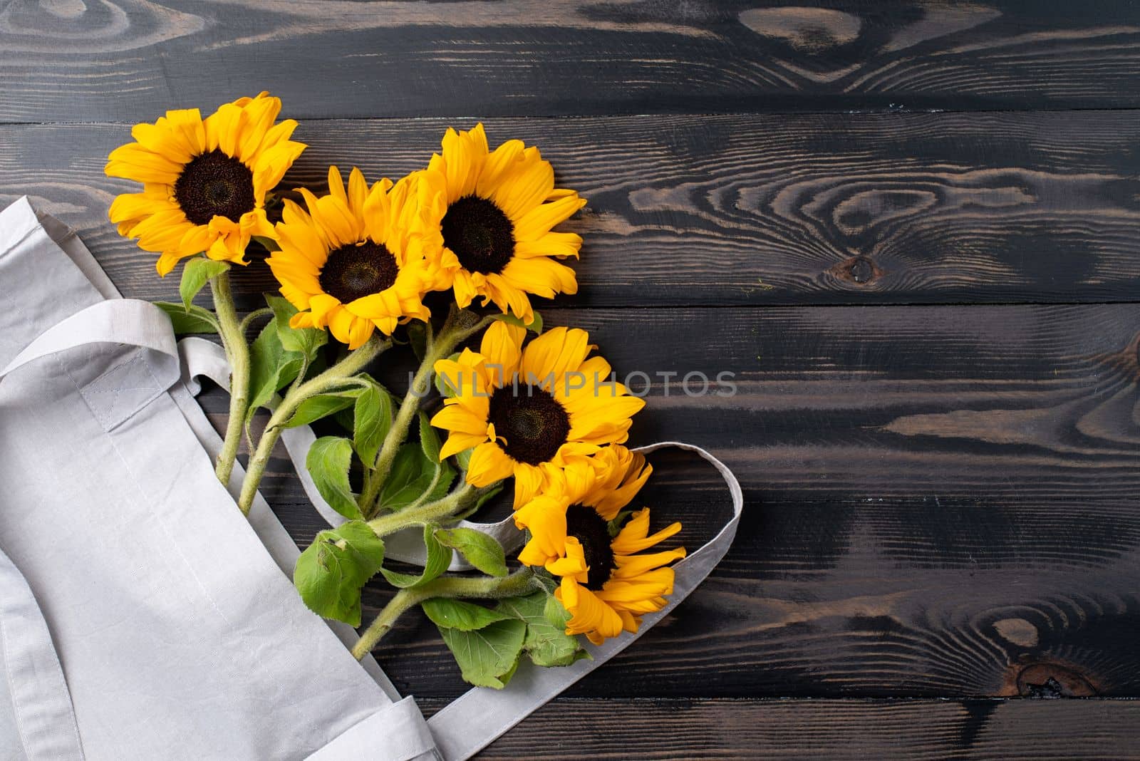 fresh sunflowers with leaves on stalk in shopping bag on wooden background. Flat lay, top view, copy space. by Desperada
