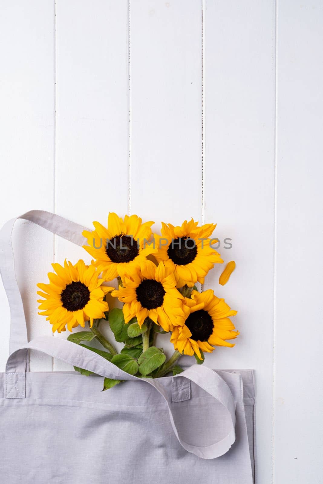 fresh sunflowers with leaves on stalk in shopping bag on wooden background. Flat lay, top view, copy space. by Desperada