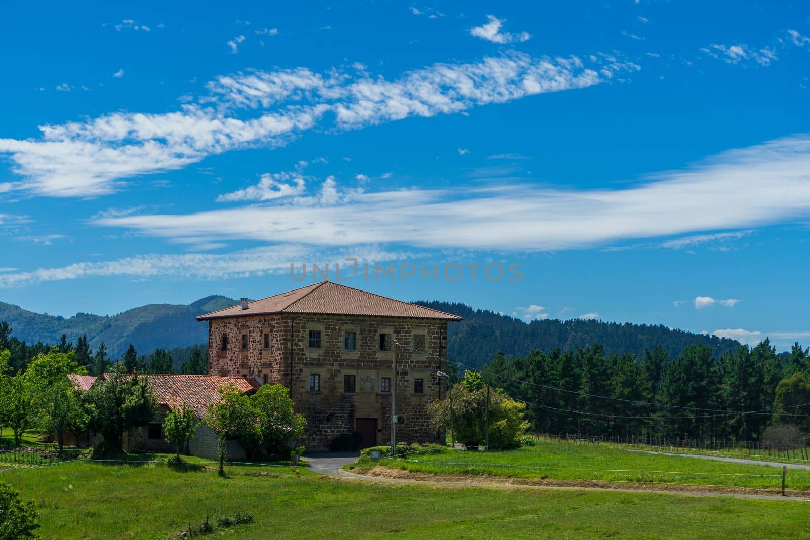 An old brick manor a tiled roof against the backdrop of mountains and green grass. Basque Country, Spain