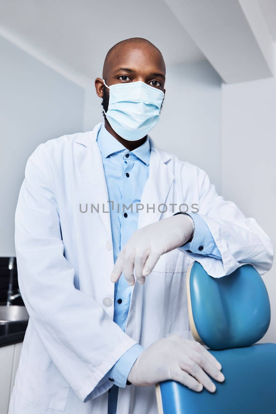 Ready to see the next patient. Portrait of a masked young man working in a dentists office. by YuriArcurs