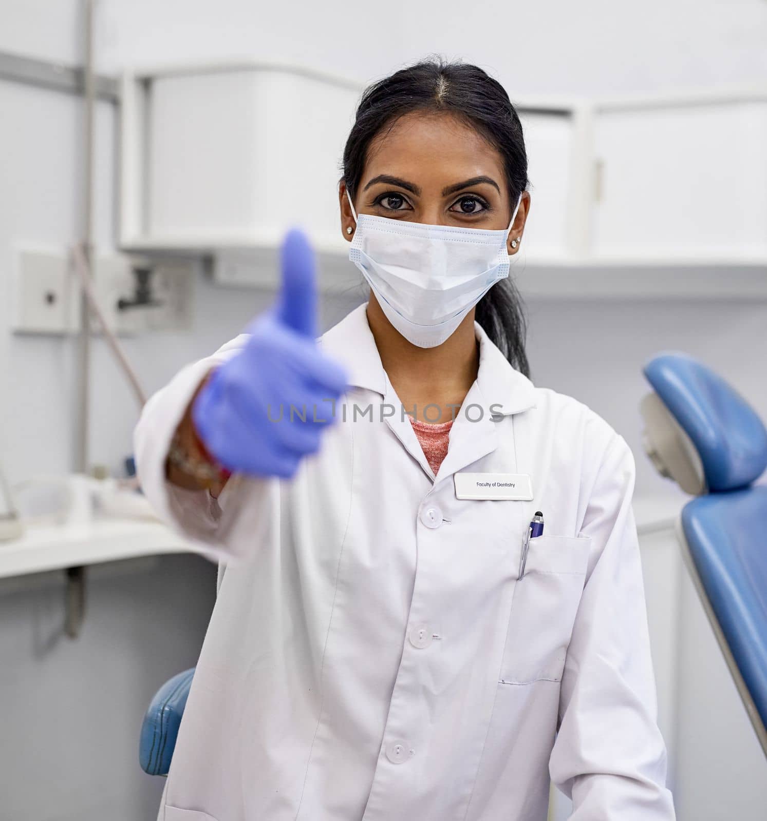 Shes got your teeth covered. Portrait of a young female dentist showing thumbs up in her office. by YuriArcurs